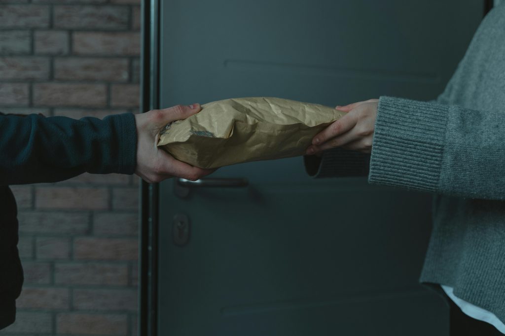 pexels-photo-6169007-6169007 Close-up of hands exchanging a package at a doorway, symbolizing home delivery service.